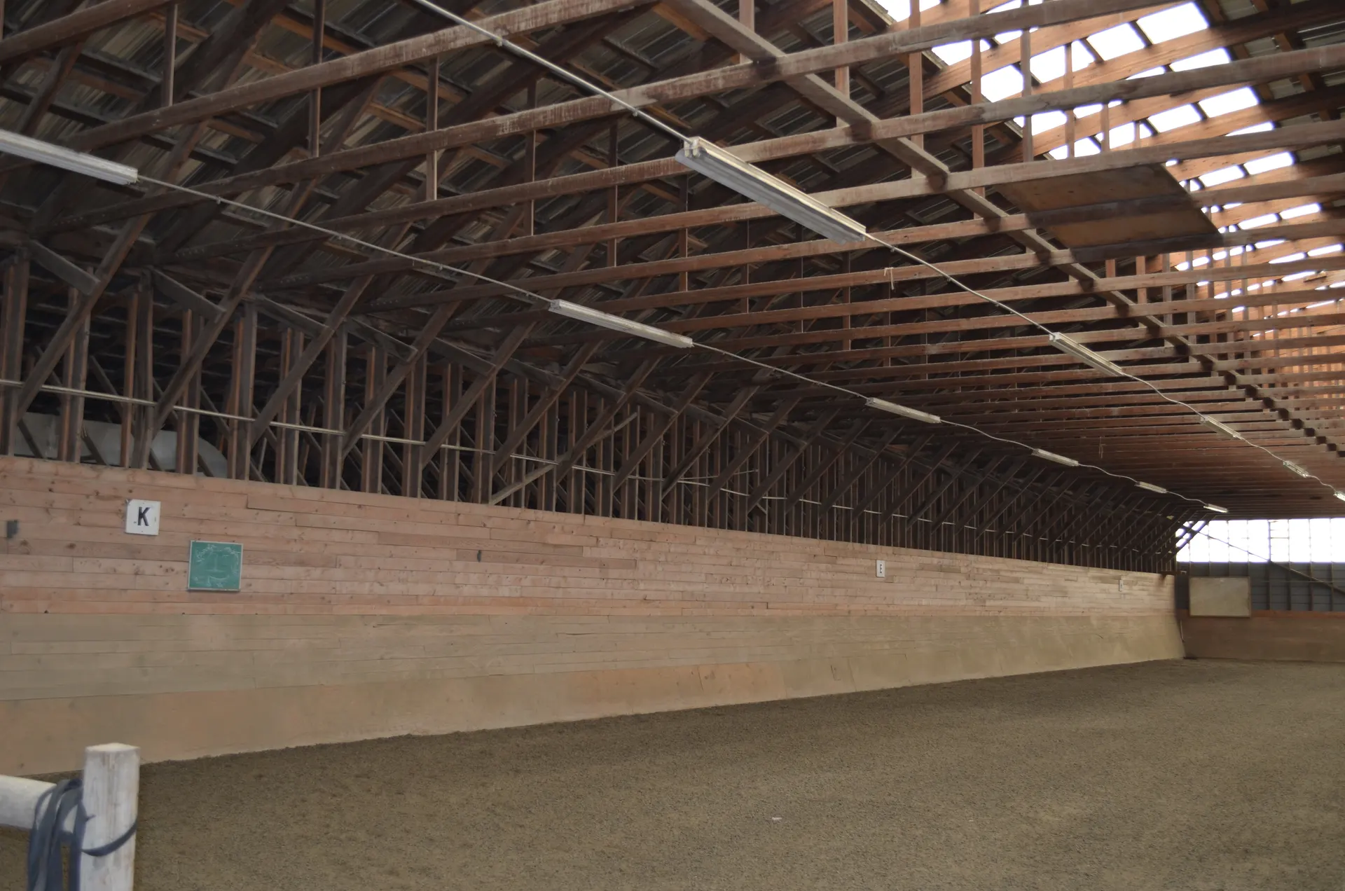 Indoor arena kickboards with dressage letters and a long timber-truss roof