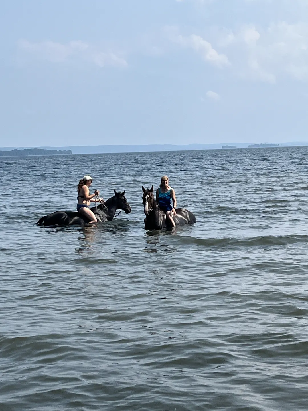 Two riders and their horses wading in the lake on a summer day