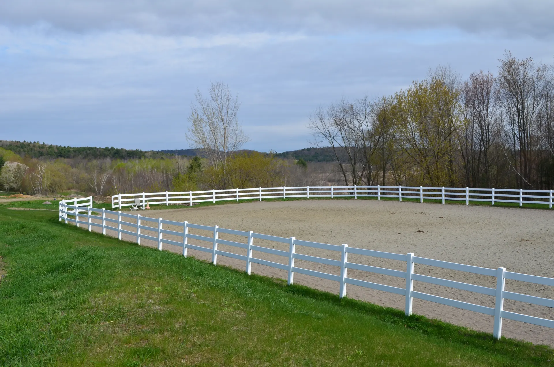 Fenced outdoor sand arena on the hilltop with white rail fencing and Vermont hills beyond