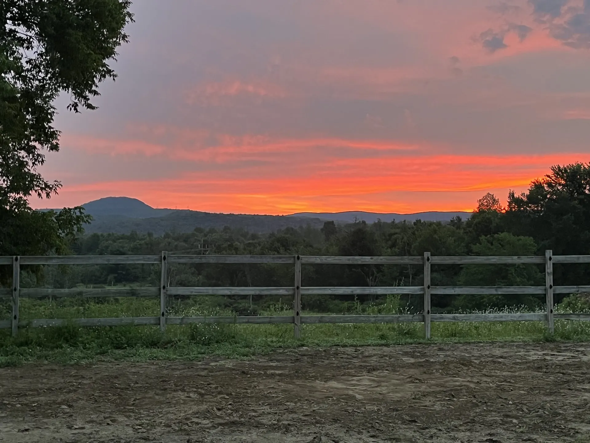 Orange sunset over the Vermont hills behind the arena rail fence